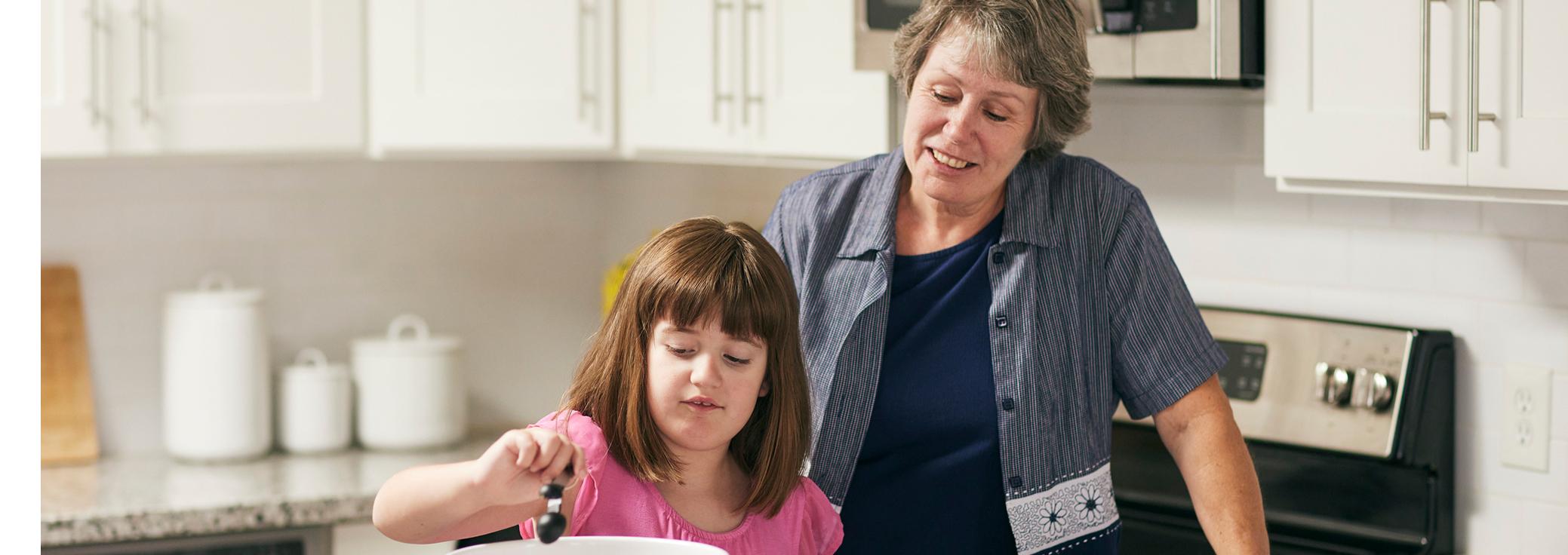 Ellamee, living with LGS, whisking bowl with grandmother standing next to her